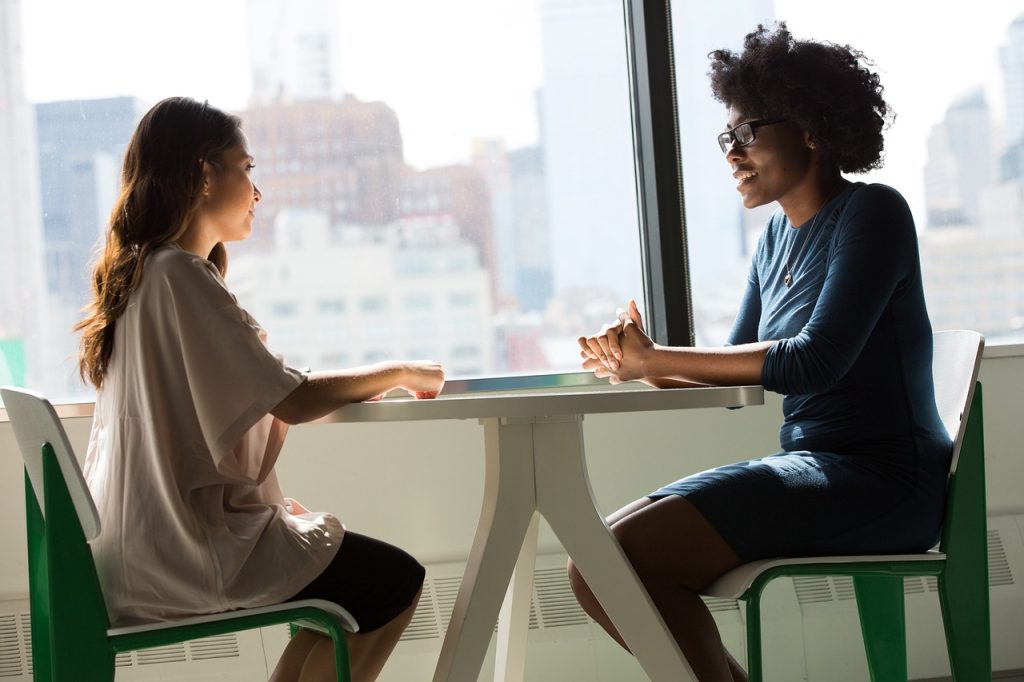 Fotografía de dos mujeres sentadas y charlando frente a frente en una mesa pequeña. Imagen de user1505195587 en Pixabay. (Español) / Fotografia de duas mulheres sentadas conversando frente a frente em uma pequena mesa. Imagem de user1505195587 no Pixabay. (Português) / Photograph of two women sitting and chatting face to face at a small table. Image by user1505195587 on Pixabay. (English)