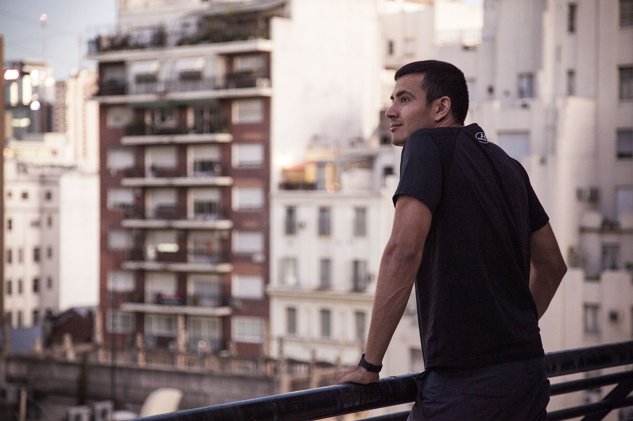 Fotografía de medio cuerpo de un hombre viendo el paisaje urbano desde una balcón. Imagen de StockSnap en Pixabay. (Español) / Half-length photograph of a man looking out over the cityscape from a balcony. / Fotografia da cintura para cima de um homem observando a paisagem urbana de uma sacada. Imagem de StockSnap no Pixabay. (Português) / Image by StockSnap on Pixabay. (English)